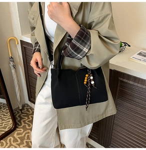 Close-up of black bucket bag with braided bead charm and elegant wavy rim edge