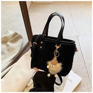Detail of black plush bucket bag with golden studs and a cute fuzzy pompom charm