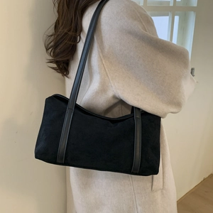 Detail of a minimalist black suede shoulder bag worn with a beige wool coat