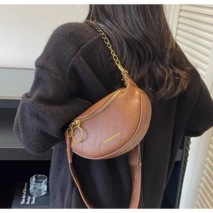 Détail d'un sac selle marron en demi-lune avec texture matelassée et chaîne dorée