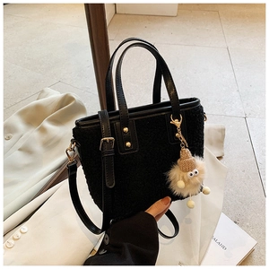 Detail of black plush bucket bag with fuzzy charm and smooth leather trim in lifestyle setting