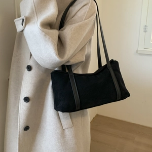 Detail view of a black suede tote bag with dual straps worn over a beige autumn coat
