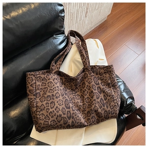 Detail of a large leopard print canvas tote bag resting on a black leather chair