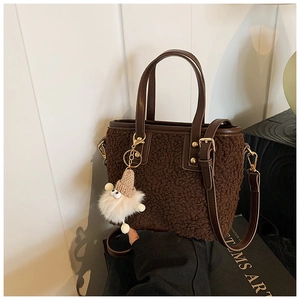 Close-up of deep brown plush bucket bag with leather handles and white pom-pom charm