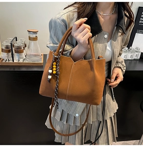 Detail view of brown pebbled leather bucket bag with a bohemian wood bead tassel charm
