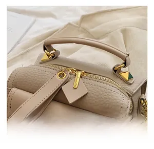 Dettaglio della borsa beige in pelle con trama litchi, zip dorata e ciondolo quadrato