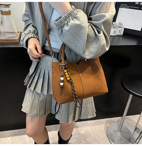 Brown leather tote bag with unique beaded charm detail and slender shoulder strap