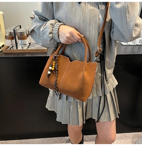 Brown suede crossbody bucket bag styled with a pleated dress and wooden bead charm