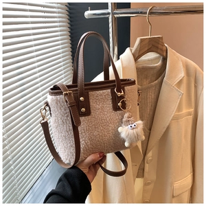 Close-up of white plush bucket bag with brown leather trim and cute bear charm