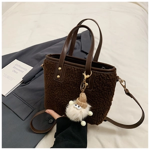 Close-up of brown plush bucket bag with leather trim and cute doll charm on a soft background