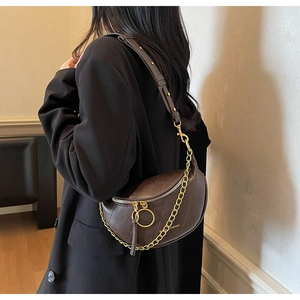 Gros plan sur un sac selle marron foncé avec chaîne dorée et logo Classic Fashion