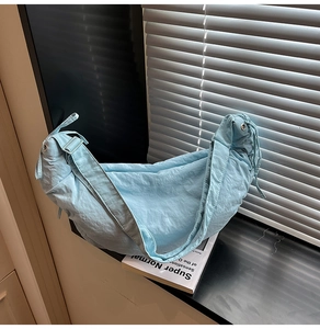 Detailed close-up of light blue pleated dumpling bag fabric with wide shoulder strap
