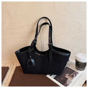 Detail of a black suede tote bag with flat leather piping and decorative hanging tag