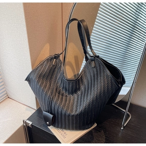 Detail of black woven leather tote bag with thick strap on a dark wooden counter