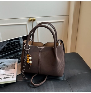 Detail of dark brown matte leather tote bag with wooden bead charm and long shoulder strap