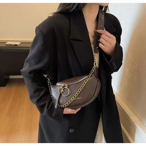Détail d'un sac demi-lune en cuir marron foncé avec chaîne dorée sur blazer noir