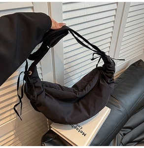 Detailed view of black pleated dumpling bag with drawstring and wide shoulder strap
