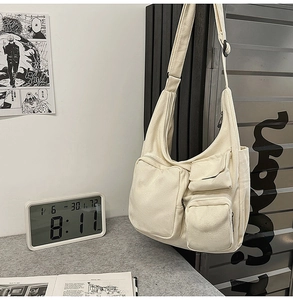 Détail du sac à bandoulière en toile blanc cassé avec plusieurs poches fonctionnelles