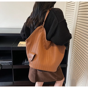 Detail of a brown woven tote bag featuring a functional side pocket with flap closure