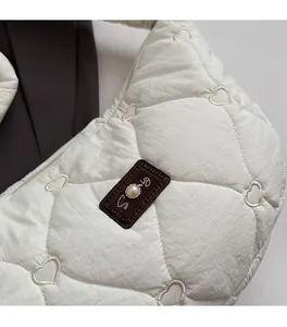 Detail of white quilted bag with heart embroidery, brown patch and pearl accent
