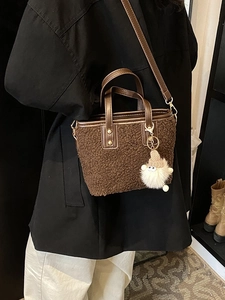 Brown plush bucket bag with cute pendant shown on a model in a casual indoor setting