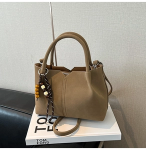 Detail view of brown matte leather handbag with vintage V-cut design and bead tassel