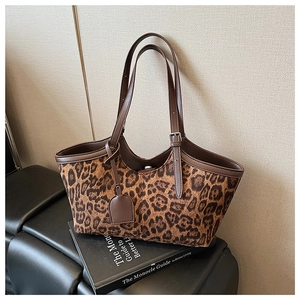Detail of leopard print tote bag with brown leather straps on a black bench