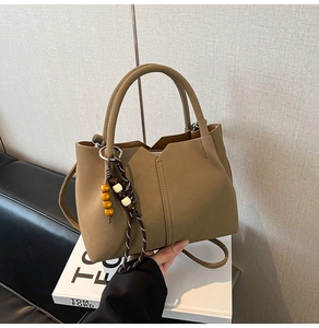 Detail of tan leather bucket bag with wooden bead charm on white decorative books