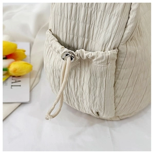 Detail of quilted drawstring side pocket on off-white tote bag with silver metal eyelets