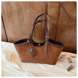 Close-up of caramel suede tote bag with brown leather handles on white fabric