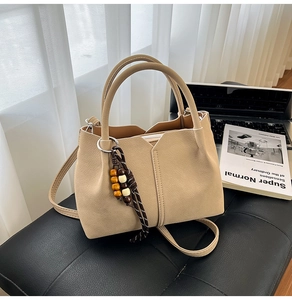 Detail of beige pebbled leather bucket bag with wooden bead charm on a leather bench