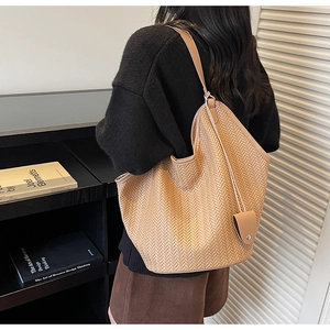 Detail of light brown woven tote bag featuring herringbone texture and shoulder strap