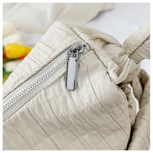 Detailed close-up of the silver metal zipper on an off-white quilted fabric tote bag
