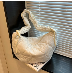 Detail of white heart-quilted puffer bag with soft padded strap on a stylish book