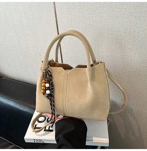 Detail of beige bucket bag with V-cut opening and ethnic beaded charm accessory