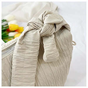 Close-up of beige pleated tote bag featuring a knotted shoulder strap and metal zipper