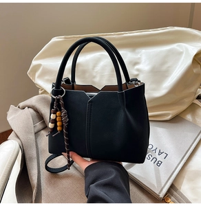 Detail of black matte tote bag featuring V-cut design and woven wooden bead tassel pendant