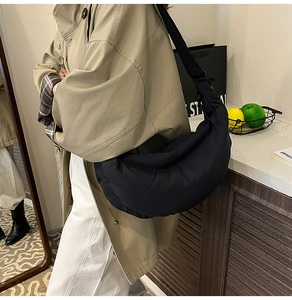 Detail of black puffy dumpling bag showing crescent shape and adjustable strap on model