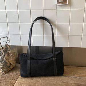 Detail view of the black suede texture and leather straps on the minimalist pillow bag