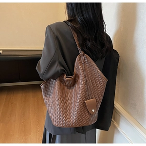 Detail of a brown woven tote bag showing the herringbone texture and small leather pouch