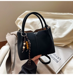 Detail view of black faux leather bucket bag with V-shaped opening and wood bead charm