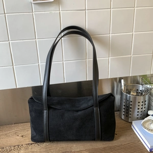 Detail of minimalist black suede pillow bag with a smooth matte texture on a wooden table