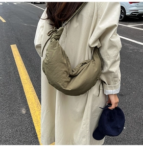 Olive green nylon dumpling bag paired with a long trench coat in an outdoor street setting