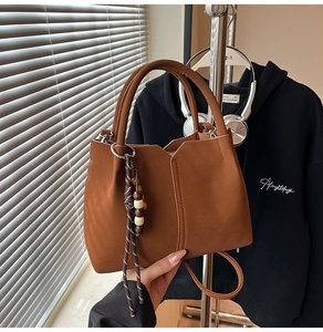 Detail of brown faux suede handbag featuring a V-cut design and woven bead charm accessory
