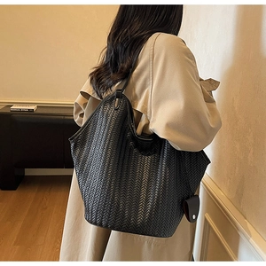 Detail of a large black woven tote bag showing the wide strap and V-pattern leather texture