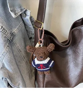 Détail d'un ours en peluche avec pull rayé accroché à un sac seau marron élégant