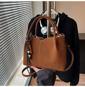 Detail of brown litchi leather bucket bag with V-cut design and woven tassel ornament
