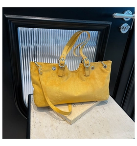 Close-up of bright yellow faux suede shoulder bag with decorative metal buckle and silver eyelets