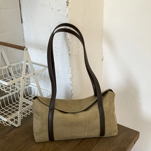 Detail view of olive green suede pillow bag with brown leather straps on wood surface