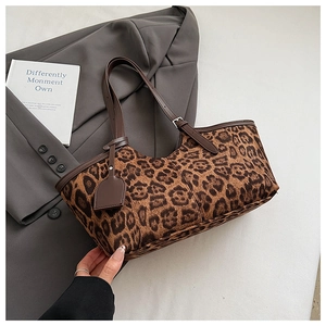 Detail of leopard print tote bag with brown leather handles on a grey suit background